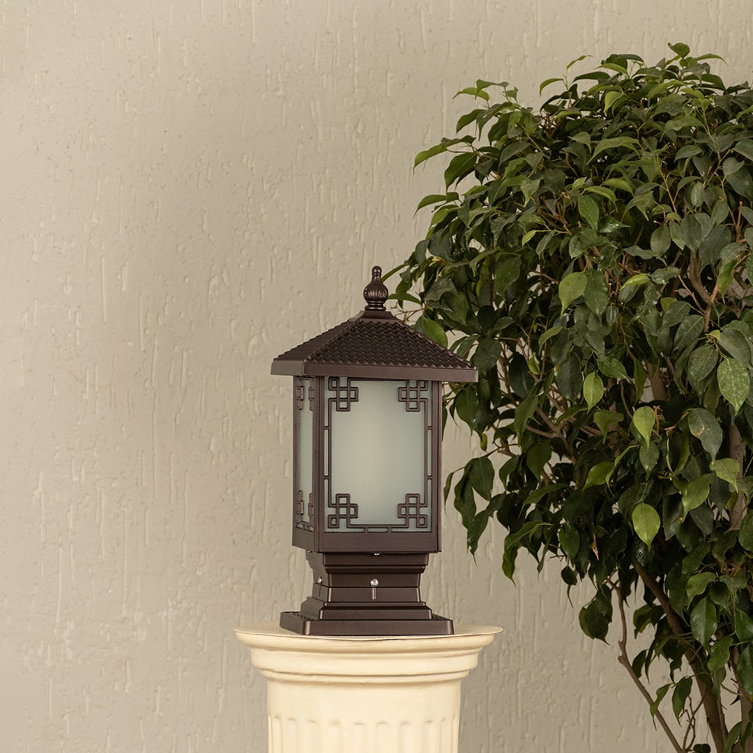 Black outdoor pillar light with ribbed glass Light On placed next to a lush green plant Lifestyle image for modern patio decor.