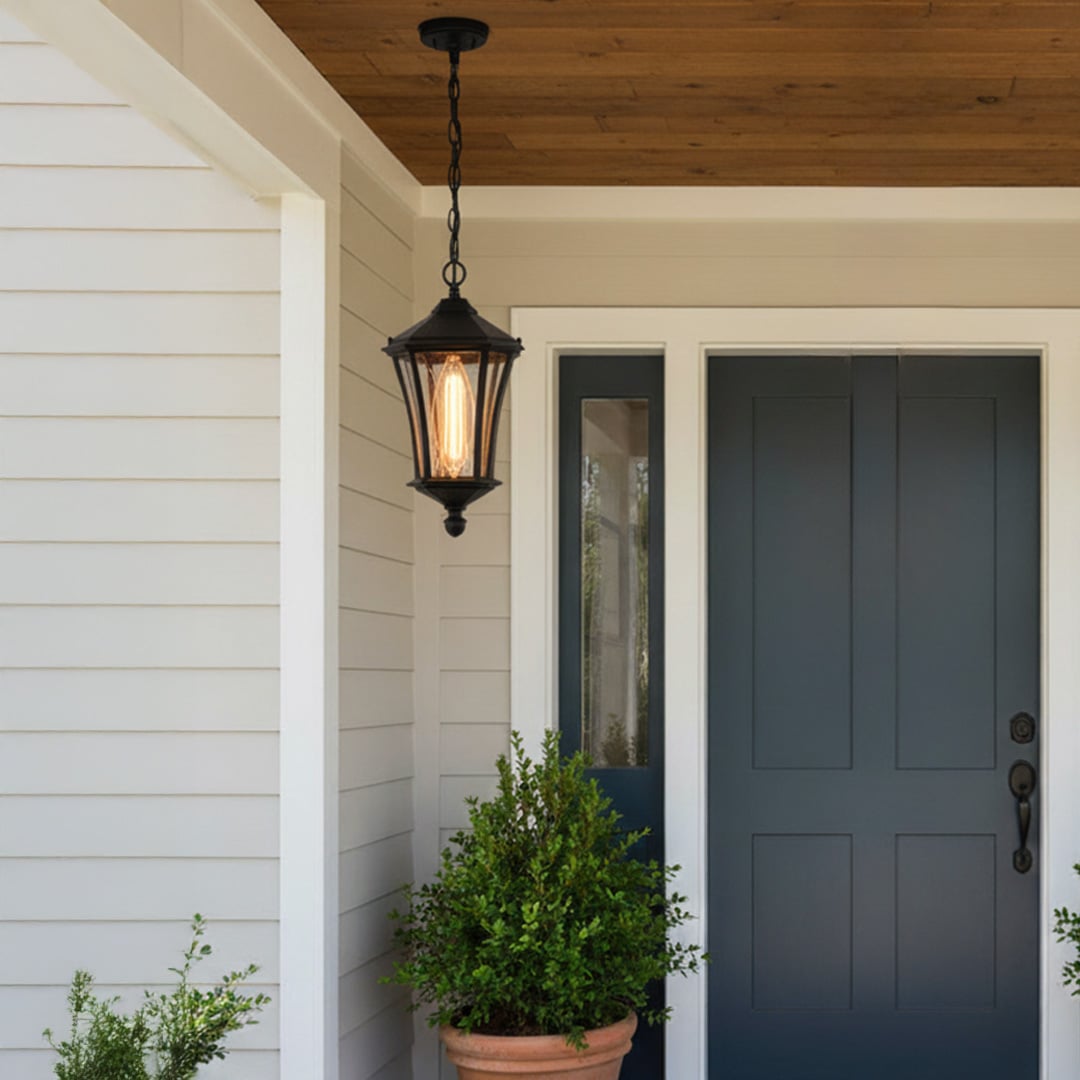 A classic black hanging outdoor lantern with warm light turned on illuminating a modern porch near a blue front door creating a welcoming ambience at the entrance at night.