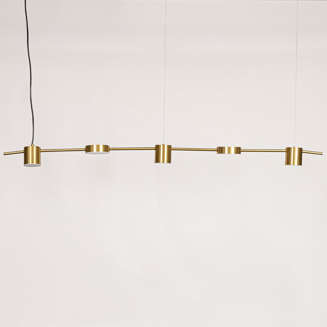Gold linear pendant light against a white background with lights off highlighting the cylindrical heads and slim linear frame in a modern design.