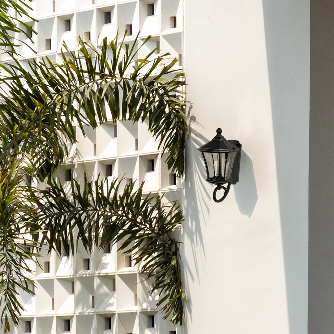 Black vintage outdoor wall lantern styled in a soft lifestyle setting with clear patterned glass and a warm glowing bulb for an elegant exterior look.