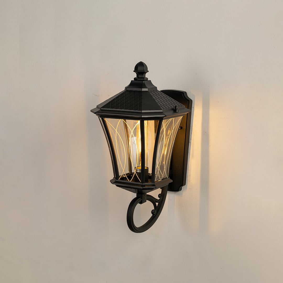 Black outdoor wall lantern displayed on a white background showing its classic frame clear patterned glass and warm interior light.