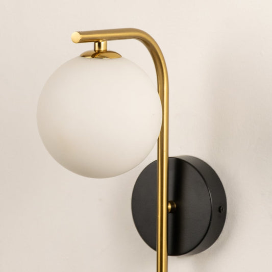 A closeup of the gold and black wall light highlighting the curved metallic arm and frosted globe shade for a refined contemporary lighting detail.
