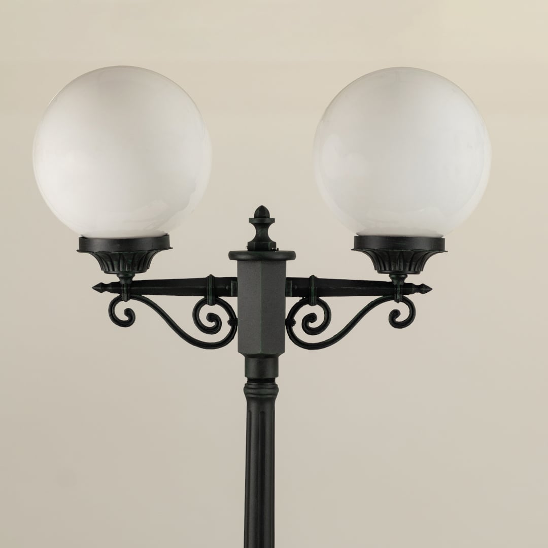 Closeup view of the double-globe lamp post showing the ornate metal detailing near the top of the pole and the smooth frosted finish of the round globes.