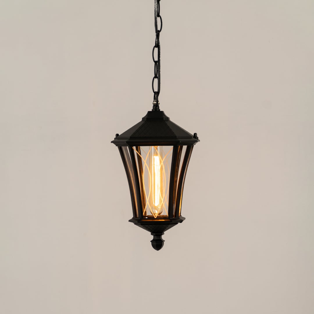 A black hanging outdoor lantern on a white background with the light turned on creating a warm glow through the clear textured glass panels.