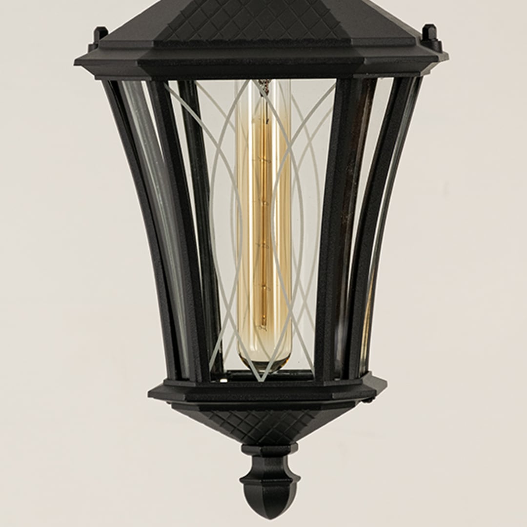 A closeup view of a black outdoor hanging lantern capturing the intricate metalwork and transparent glass panels with visible bulb detailing.