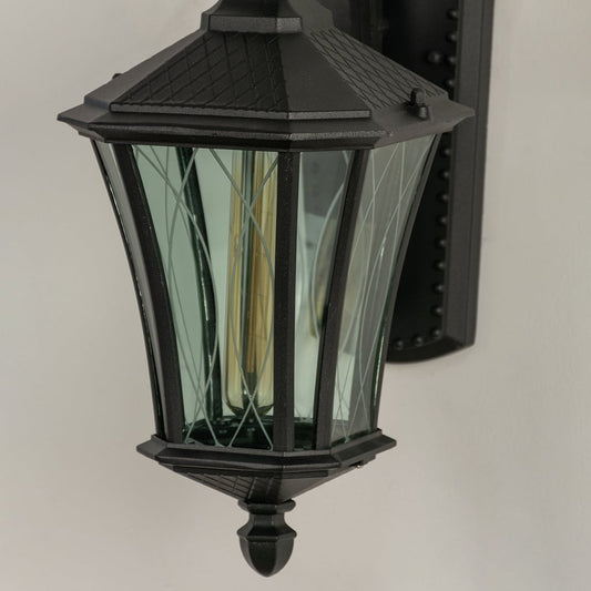Closeup of black metal outdoor lantern showing textured glass panels and elegant curved arm for refined exterior lighting.