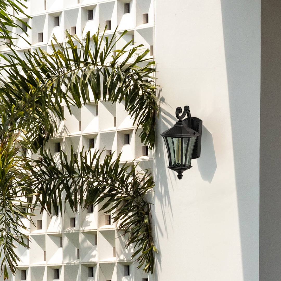 Black metal outdoor wall lantern with curved arm and textured glass mounted on a bright exterior wall adding classic architectural outdoor styling.