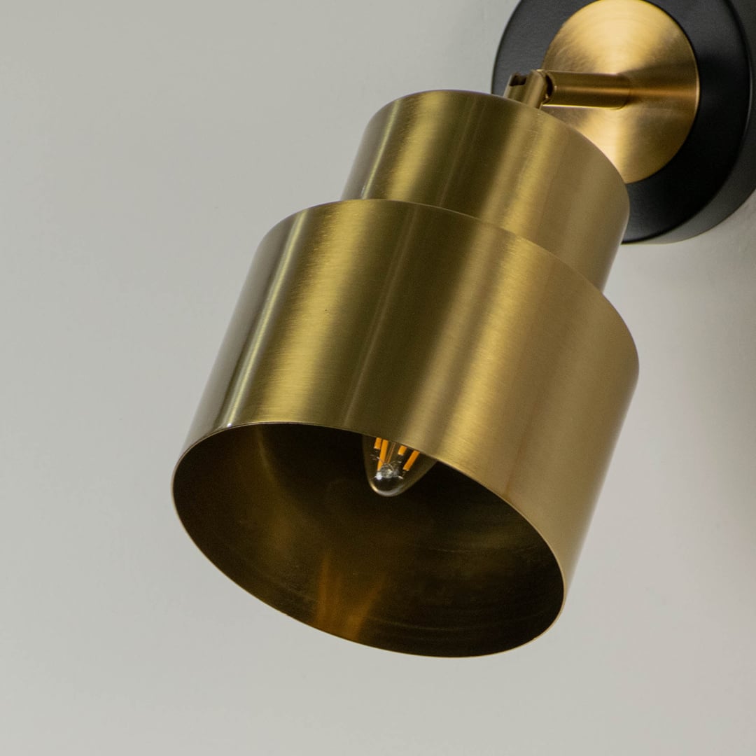 Close up of a gold wall light with a layered design black accents and exposed bulb emphasizing its sleek and contemporary style.