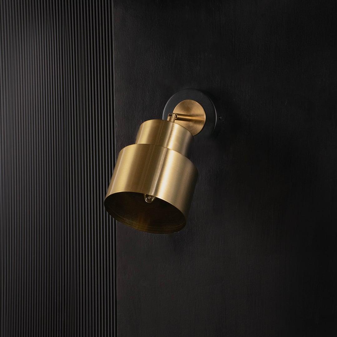 Gold and black wall-mounted light displayed without illumination against a black background emphasizing its sleek and layered design.