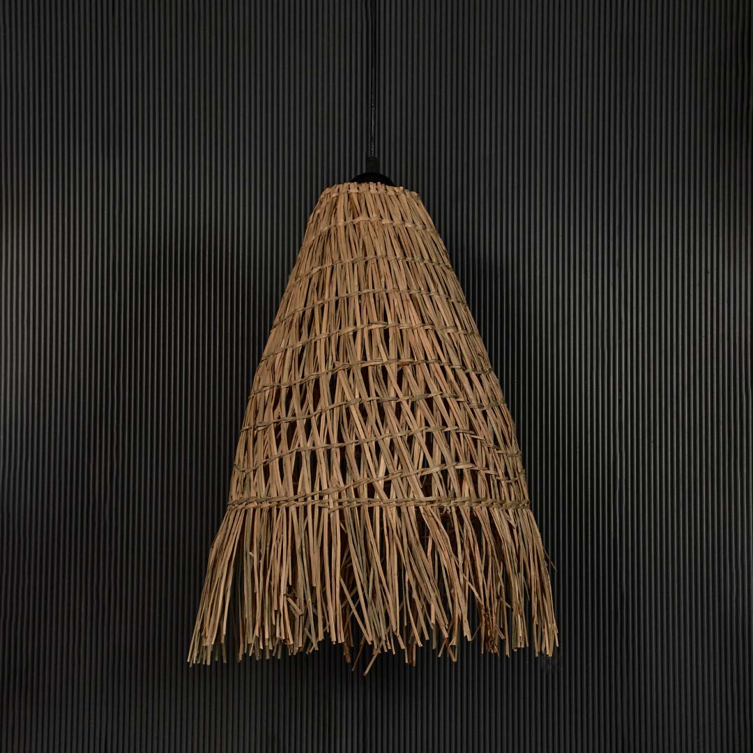 Rattan pendant light with tall woven shade and fringed edge shown off on black background for rustic home decor.