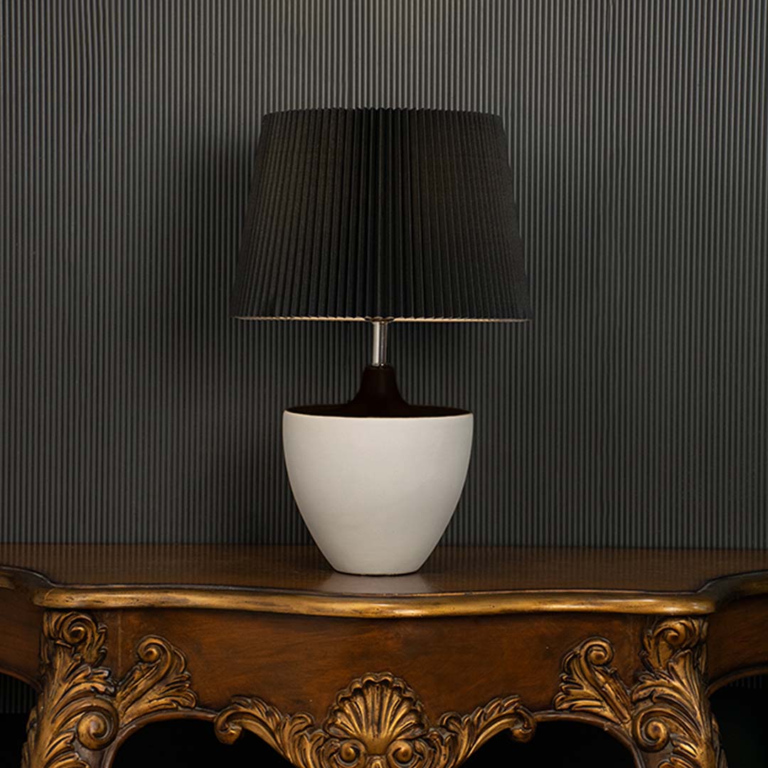 Black table lamp with pleated shade and white base shown unlit on a dark backdrop for contrast and texture focus.