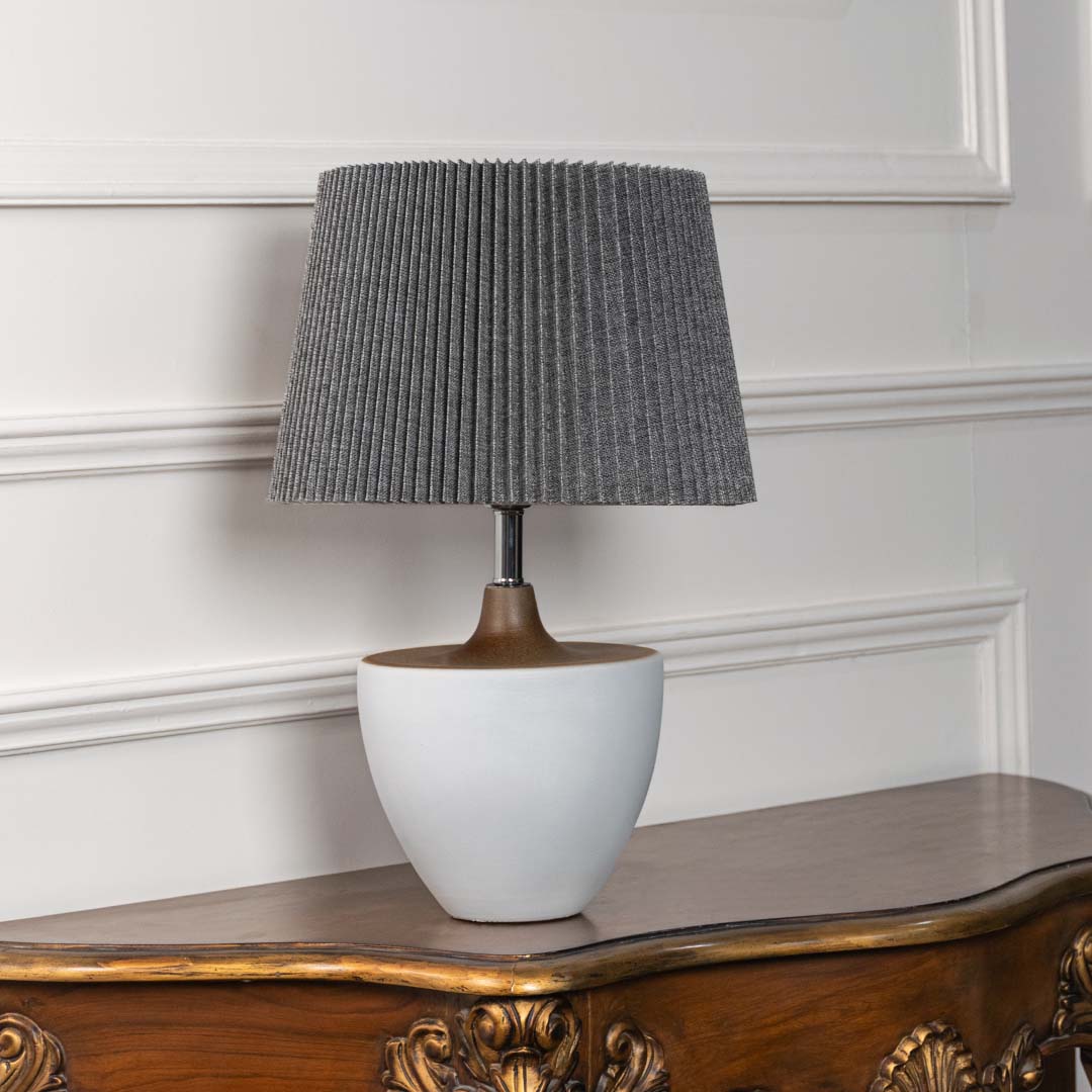 White ceramic lamp with grey pleated shade shown unlit on a plain white background showcasing its simple elegant modern shape.