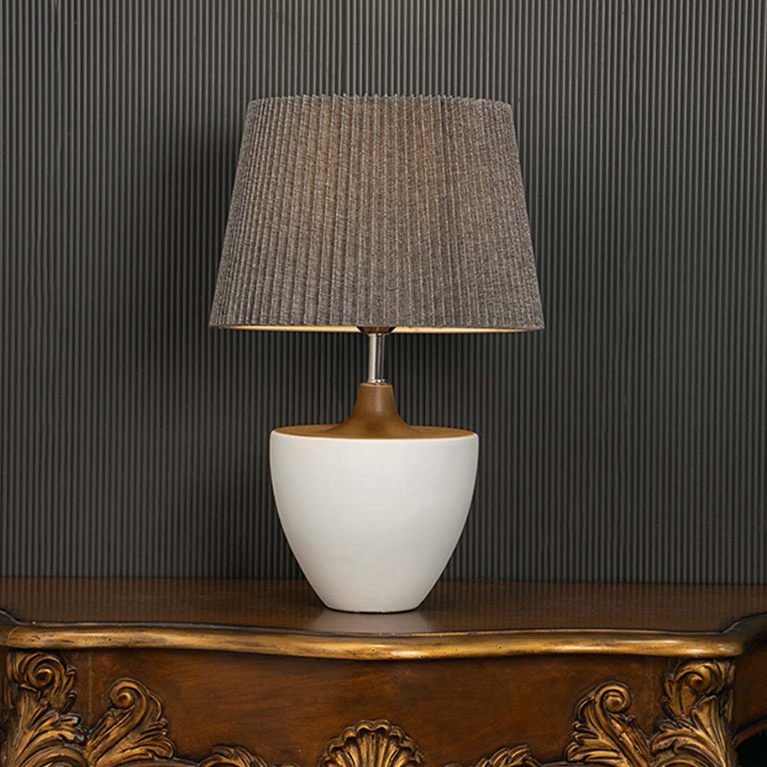 Grey pleated lamp with glowing warm light and white ceramic base highlighted on a dark background creating a bold stylish decor accent.