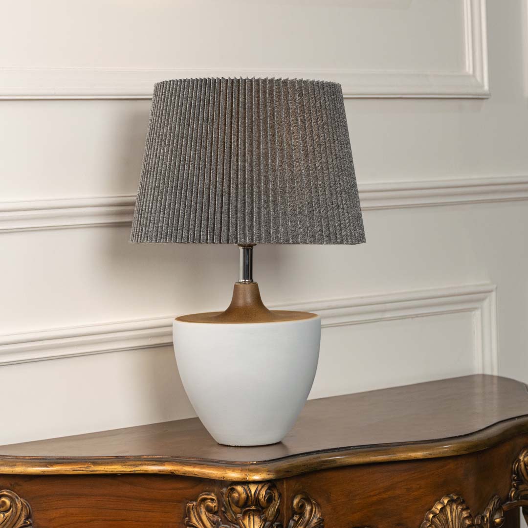 White ceramic table lamp with grey pleated shade glowing softly on a white background highlighting its clean modern decorative design.