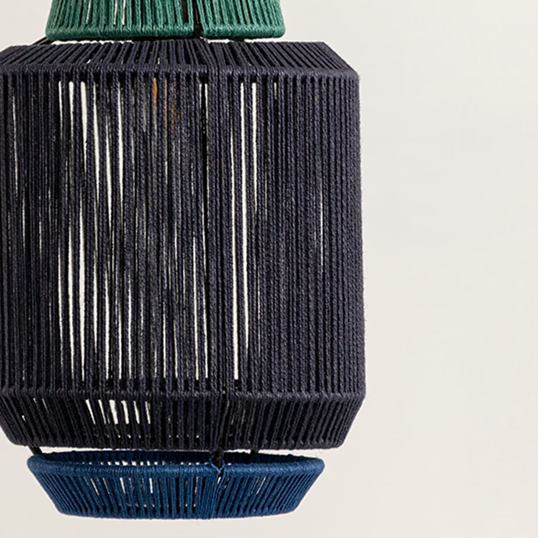 A pendant light with a dark woven cylindrical shade and subtle textural detail glowing warmly and adding a handcrafted natural focal accent to the surrounding interior.