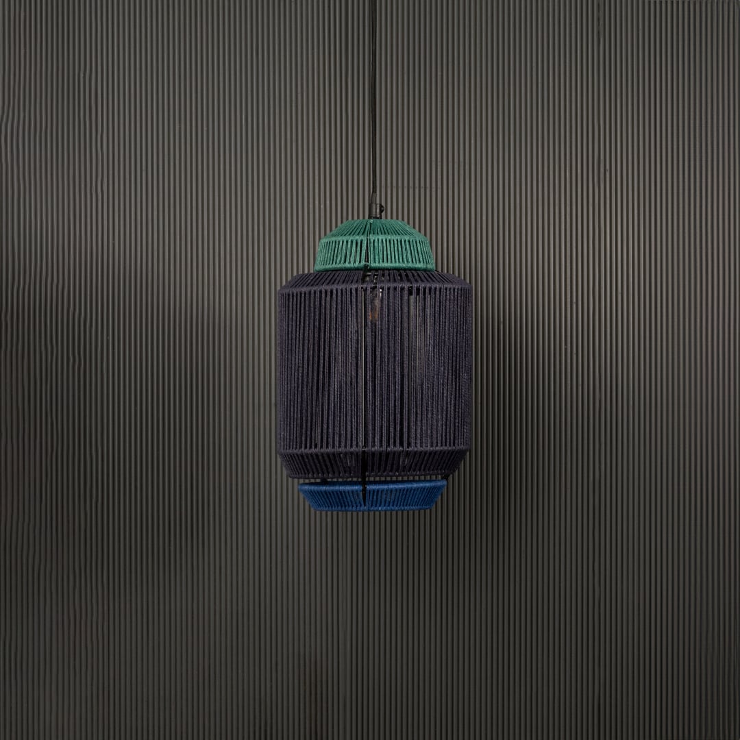 Pendant light with a dark woven cylindrical shade and green top glowing softly against a dark backdrop adding a natural handcrafted highlight that enriches the room atmosphere.