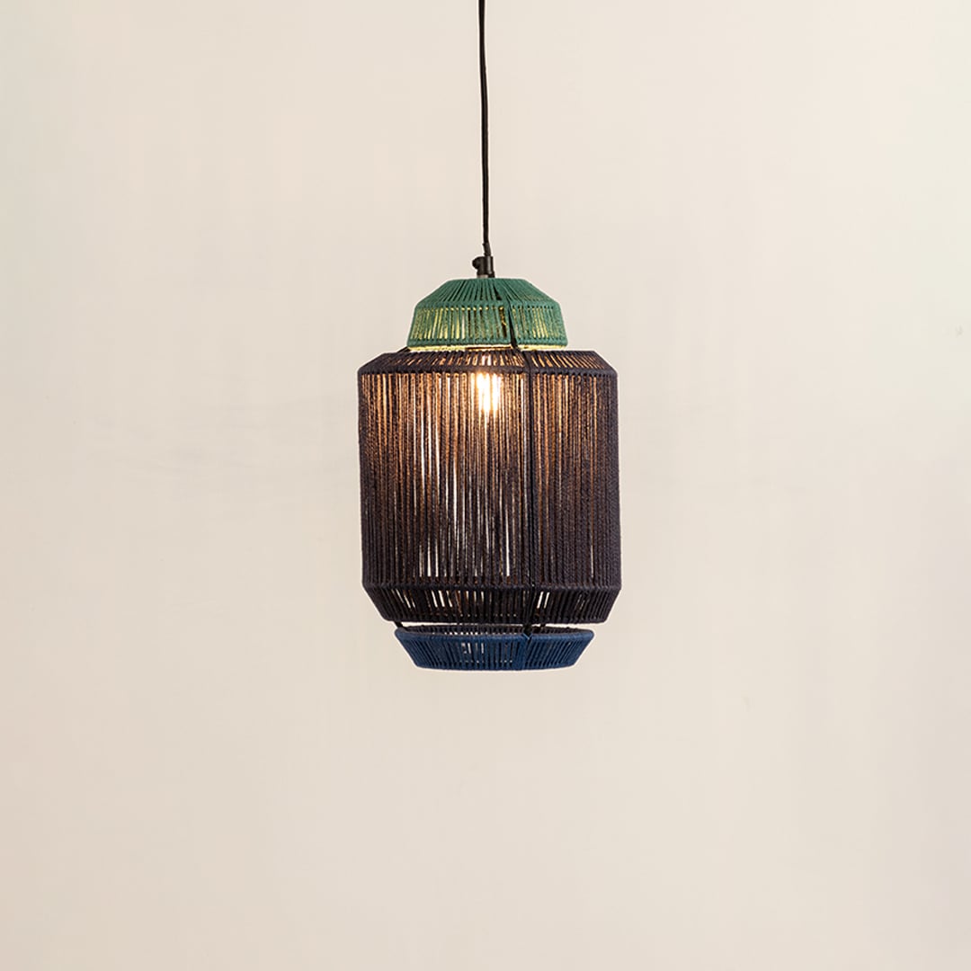 Pendant light with a green top and textured dark woven shade creating a warm soft glow that brings a natural handcrafted feel to the surrounding interior space.