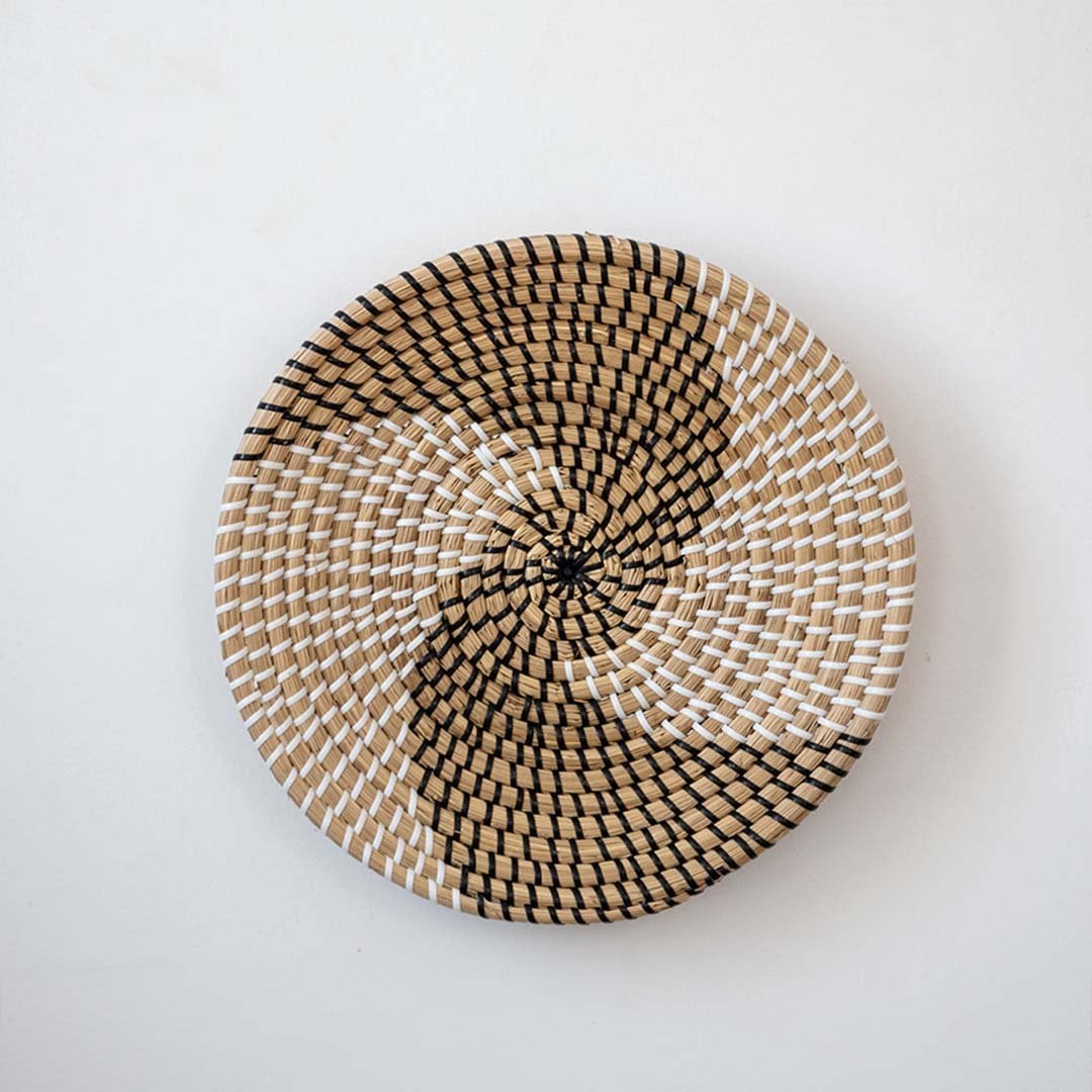 Handwoven wicker basket wall decor in beige with black and white spiral woven pattern design on clean white background.