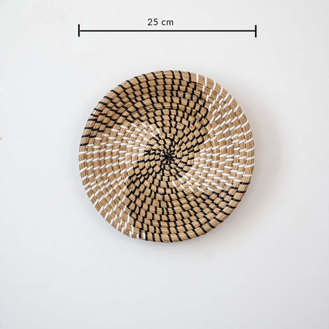 Handwoven wicker basket wall decor in beige with black spiral woven pattern showing 25 cm size measurement on white.