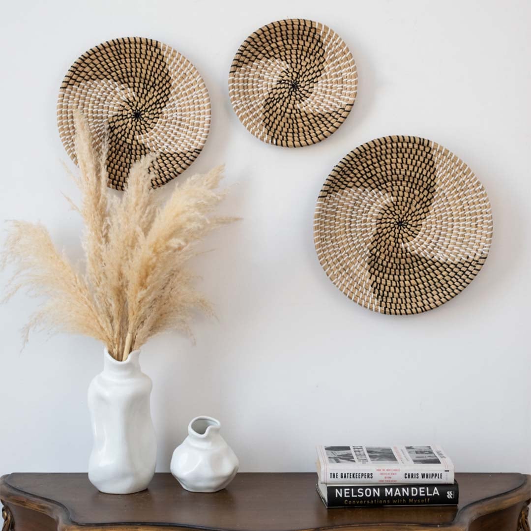 Handwoven wicker basket wall decor styled with pampas grass vase and books on wooden console for boho home interiors.