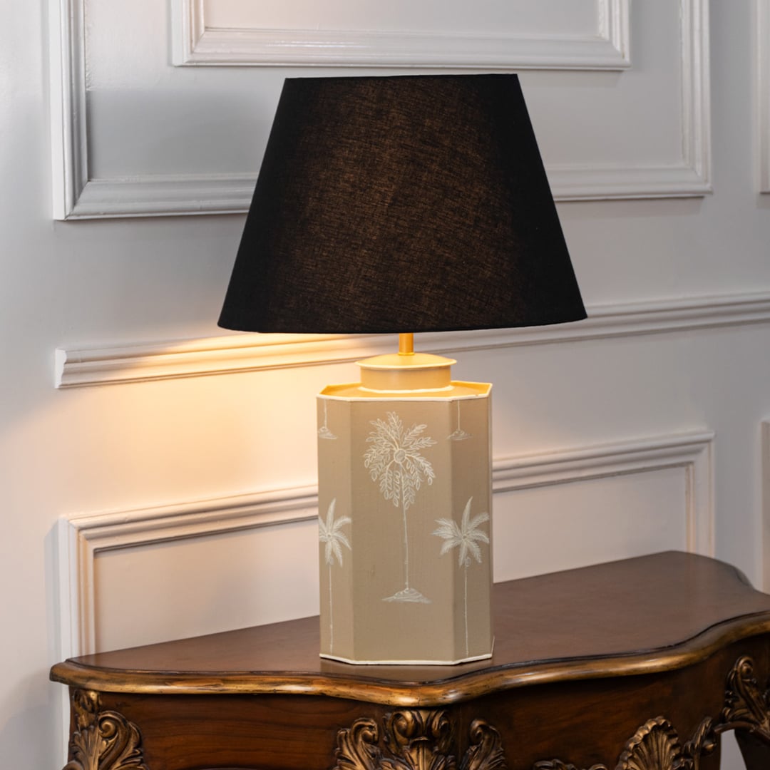 Palm tree table lamp turned on with warm light featuring beige ceramic base and black fabric shade ideal for cozy bedroom or living room lighting.