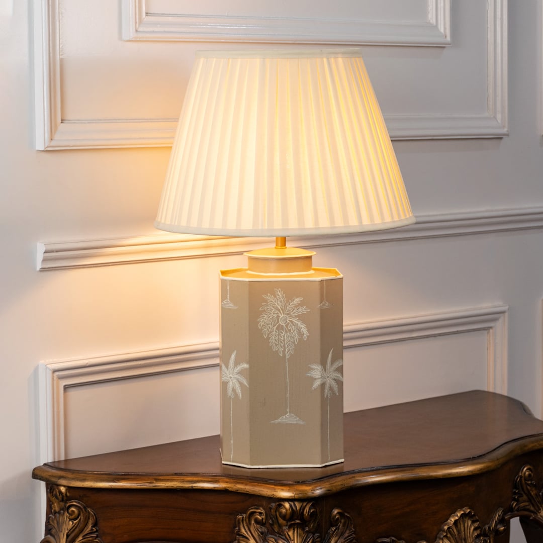 Palm tree table lamp turned on with warm yellow light featuring beige ceramic base and pleated cream shade perfect for elegant living room decor.