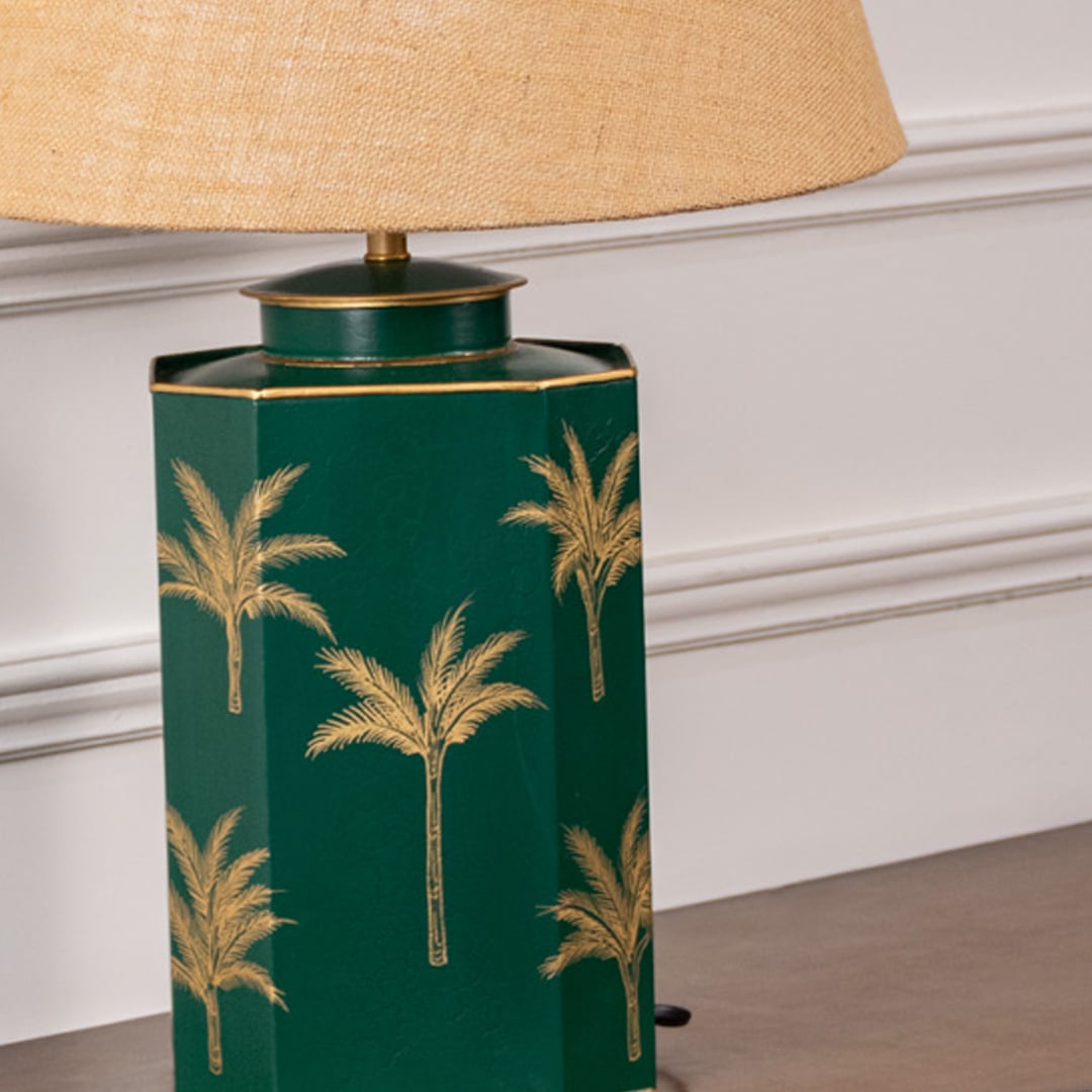 Closeup of green palm table lamp highlighting intricate golden palm pattern on glossy green ceramic base adding tropical sophistication to interior spaces.