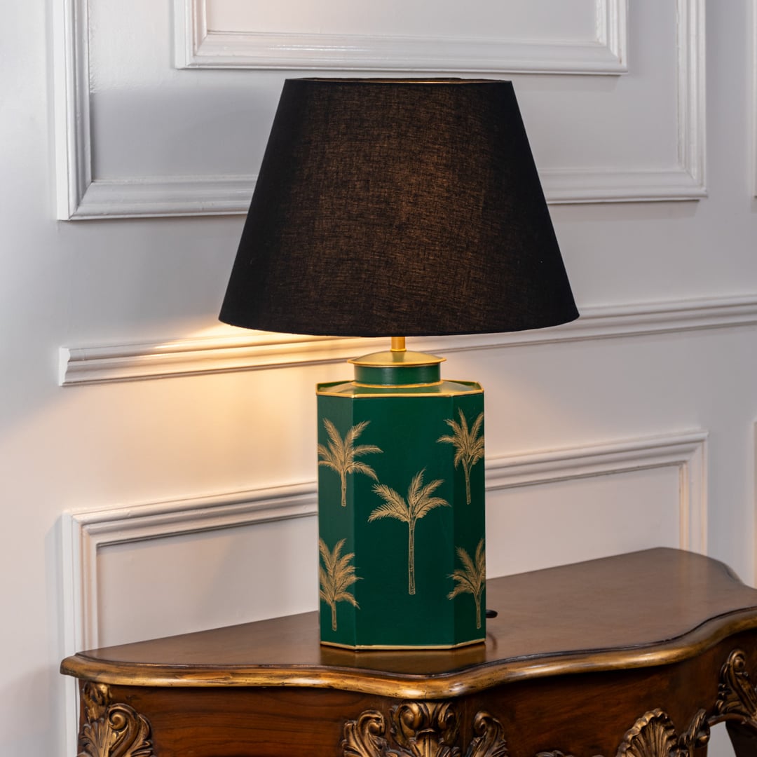 Green palm table lamp turned on with warm soft glow featuring golden palm motifs on green ceramic base and black shade perfect for elegant home lighting decor.