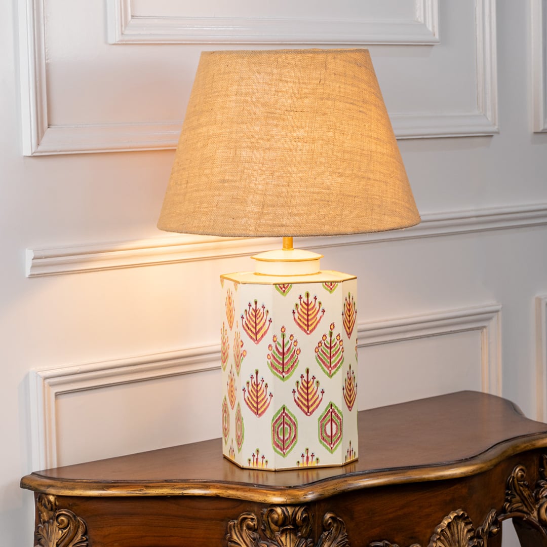 Ceramic table lamp with beige jute shade glowing gently against a clean white background. The hand painted floral pattern and cream base create a premium look perfect for modern living rooms bedrooms and reading corners.