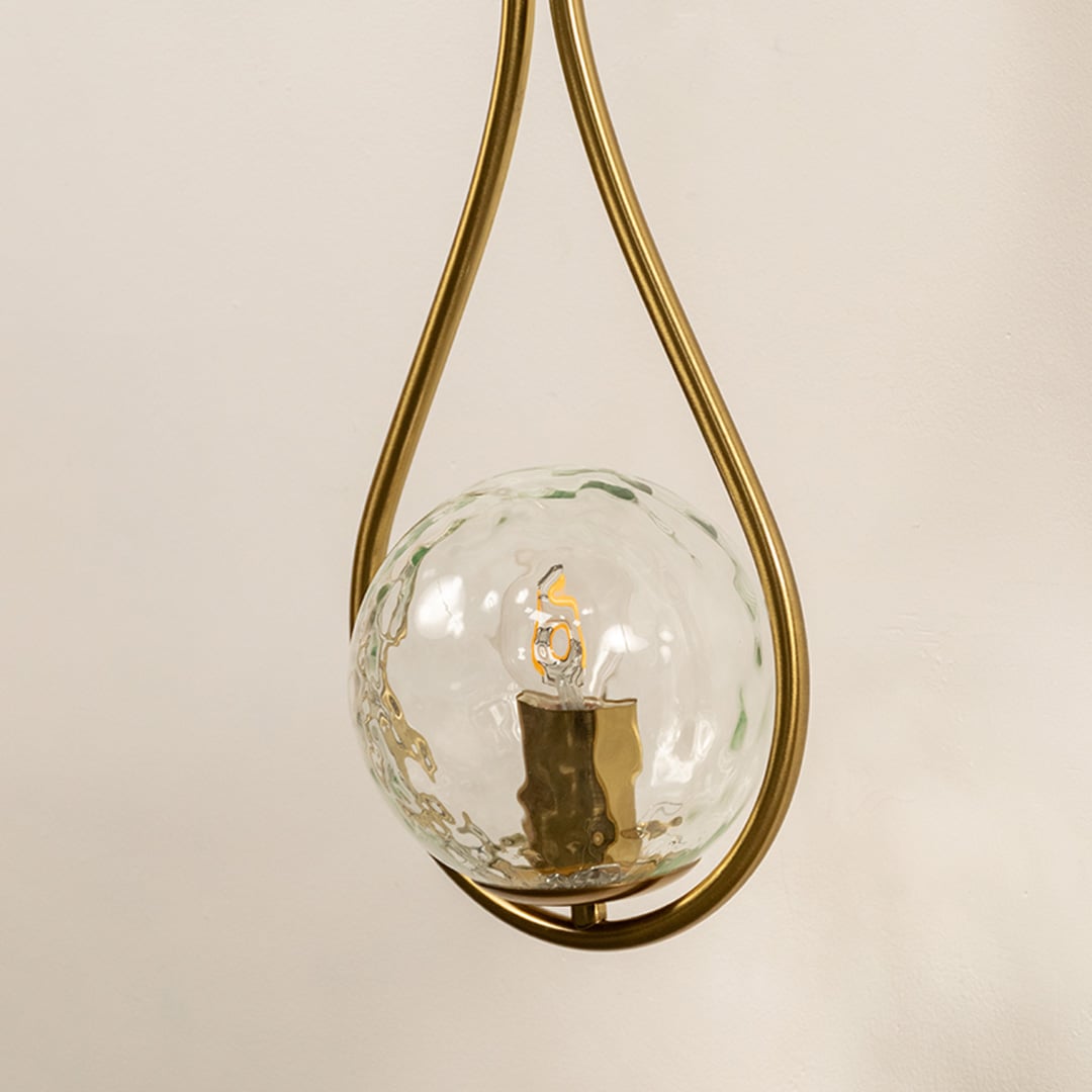 Closeup of brushed gold teardrop wall light showing detailed hammered glass globe and curved metallic frame ideal for modern home decor.
