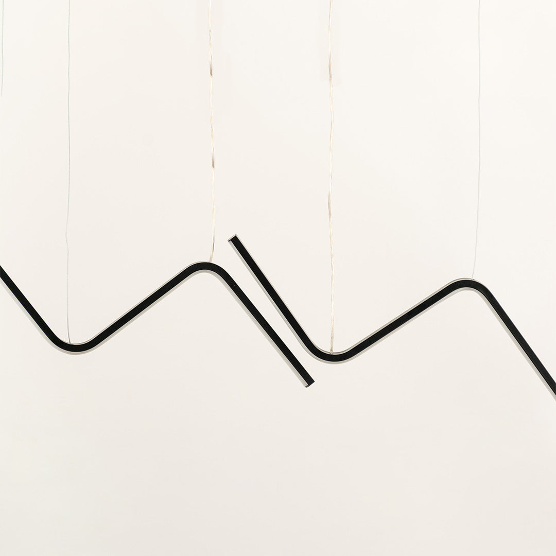 Black sculptural chandelier with flowing wave shaped LED bars suspended horizontally creating a bold artistic lighting statement across the interior wall.