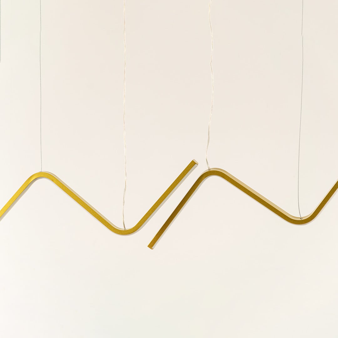 Gold sculptural chandelier featuring sweeping wave shaped LED bars suspended elegantly creating a warm dynamic decorative lighting accent in the modern room.
