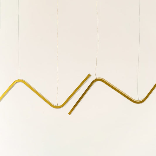 Gold sculptural chandelier featuring sweeping wave shaped LED bars suspended elegantly creating a warm dynamic decorative lighting accent in the modern room.