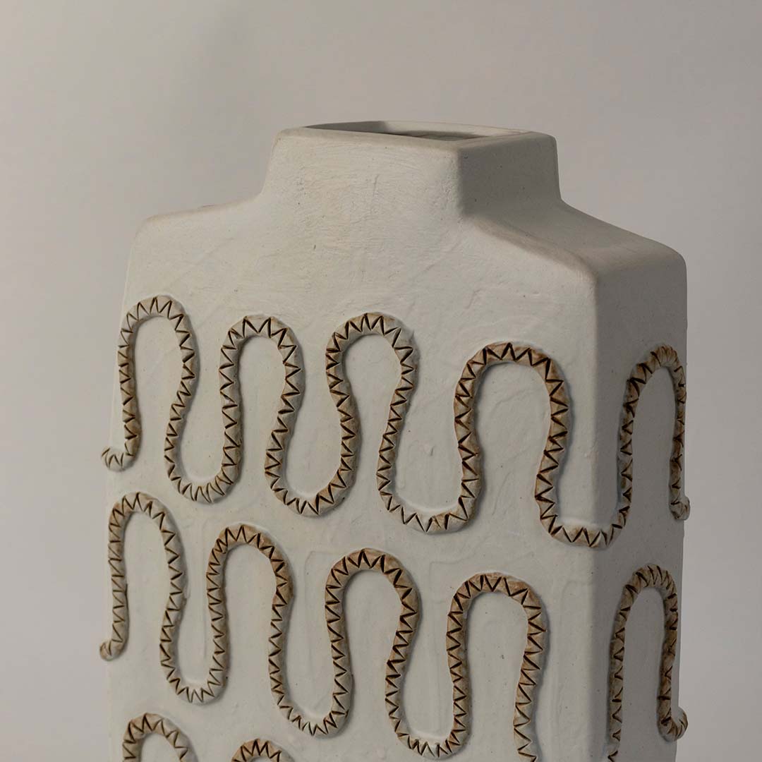 Closeup of handcrafted tall white ceramic vase with detailed zigzag textured carving highlighting artistic craftsmanship.