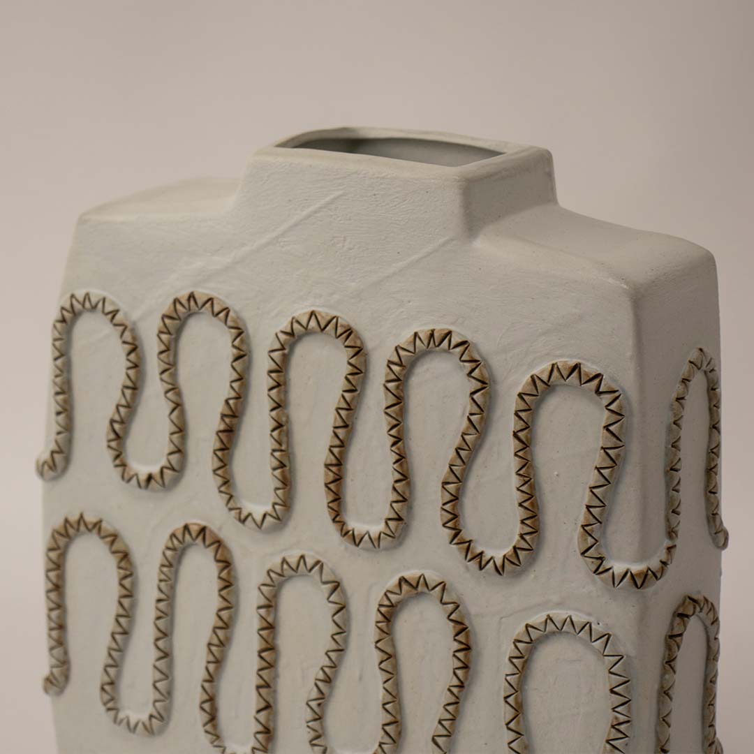 Closeup of handcrafted white ceramic vase with detailed zigzag textured carving highlighting artistic craftsmanship for interiors.