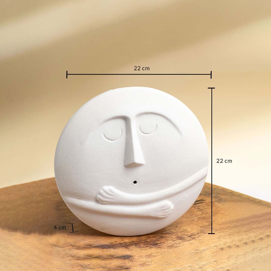 Round white ceramic face vase measuring 22 cm in height 22 cm in width and 4 cm in depth with embossed facial details and hugging arms.
