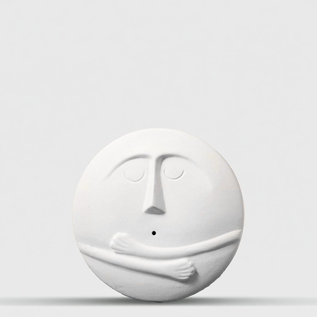 Minimal round white ceramic face vase with closed-eye expression and subtle texture placed on a smooth neutral backdrop.