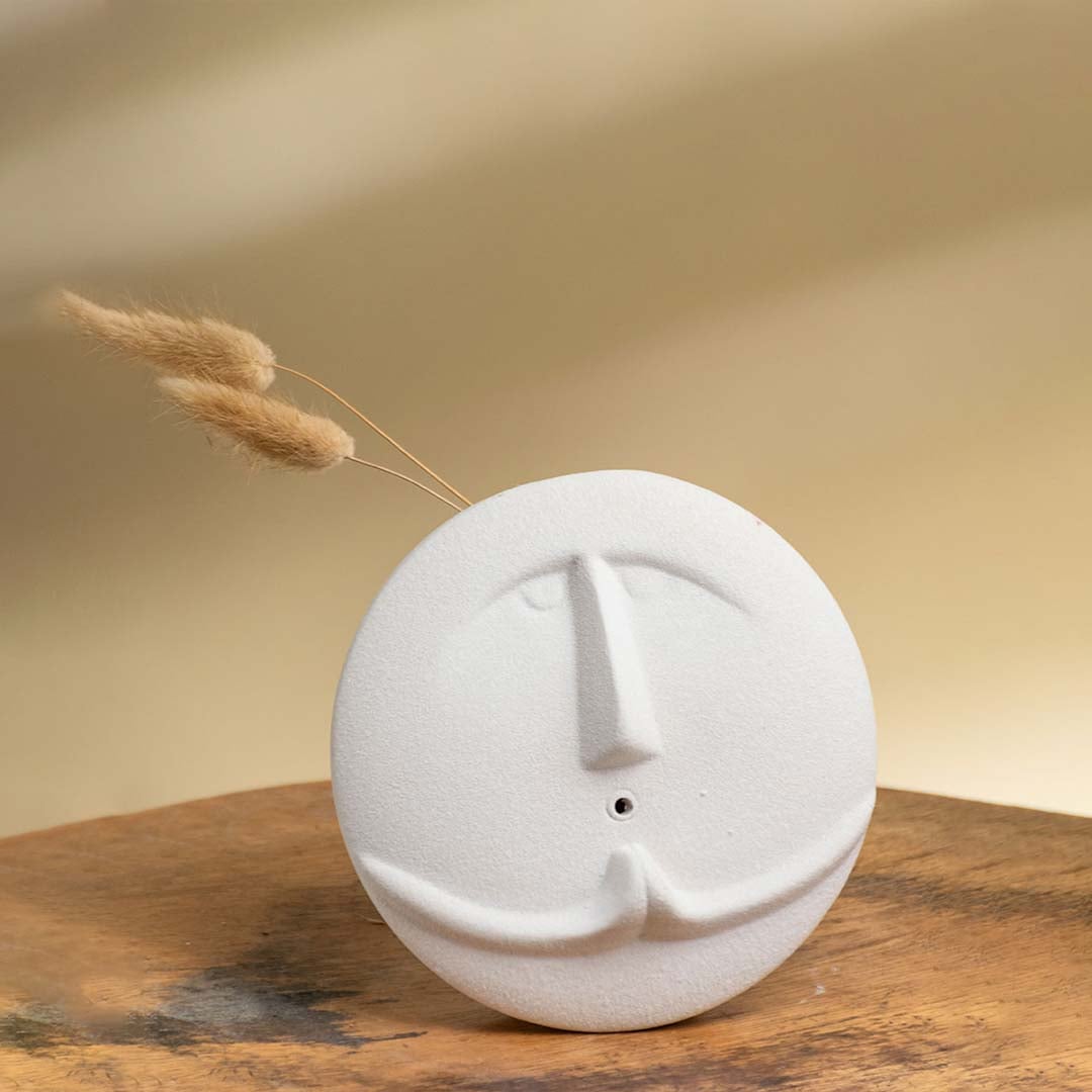 Round white face vase with a sculpted nose and mustache placed on a wooden surface in warm soft lighting creating a cozy decor look.