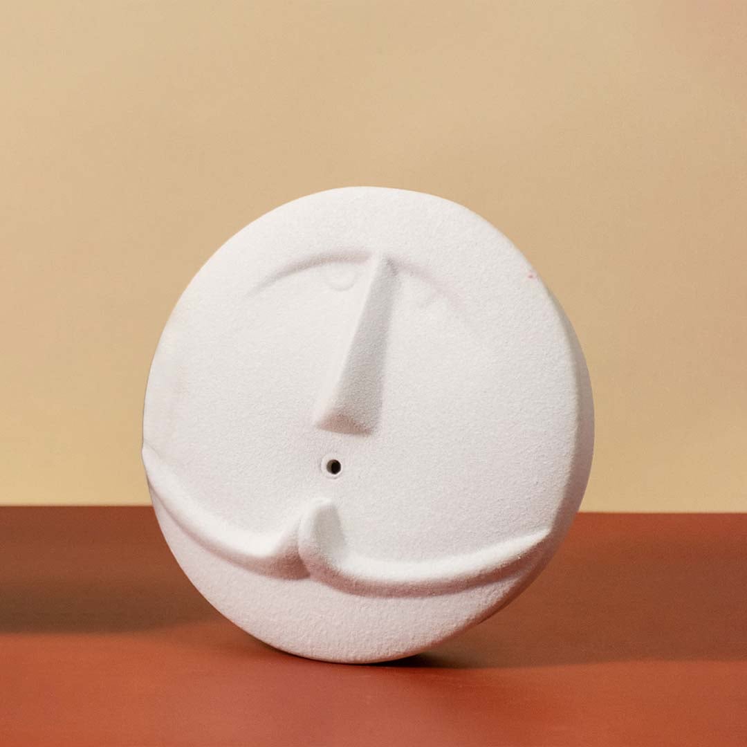 Round white face sculpture vase standing against a clean light background highlighting its smooth texture and artistic carved facial details.