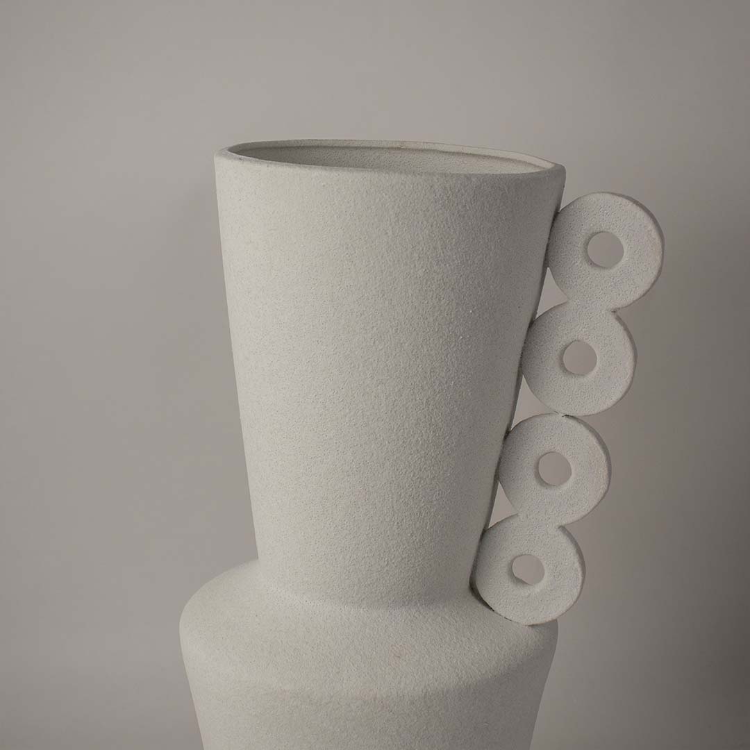 Closeup of matte white ceramic vase showing its circular handle detailing and fine handcrafted surface texture.