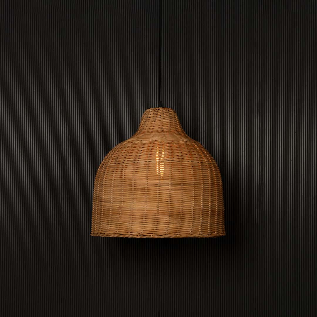 Brown rattan pendant light with dome-shaped bamboo weave turned on glowing softly against plain black background.