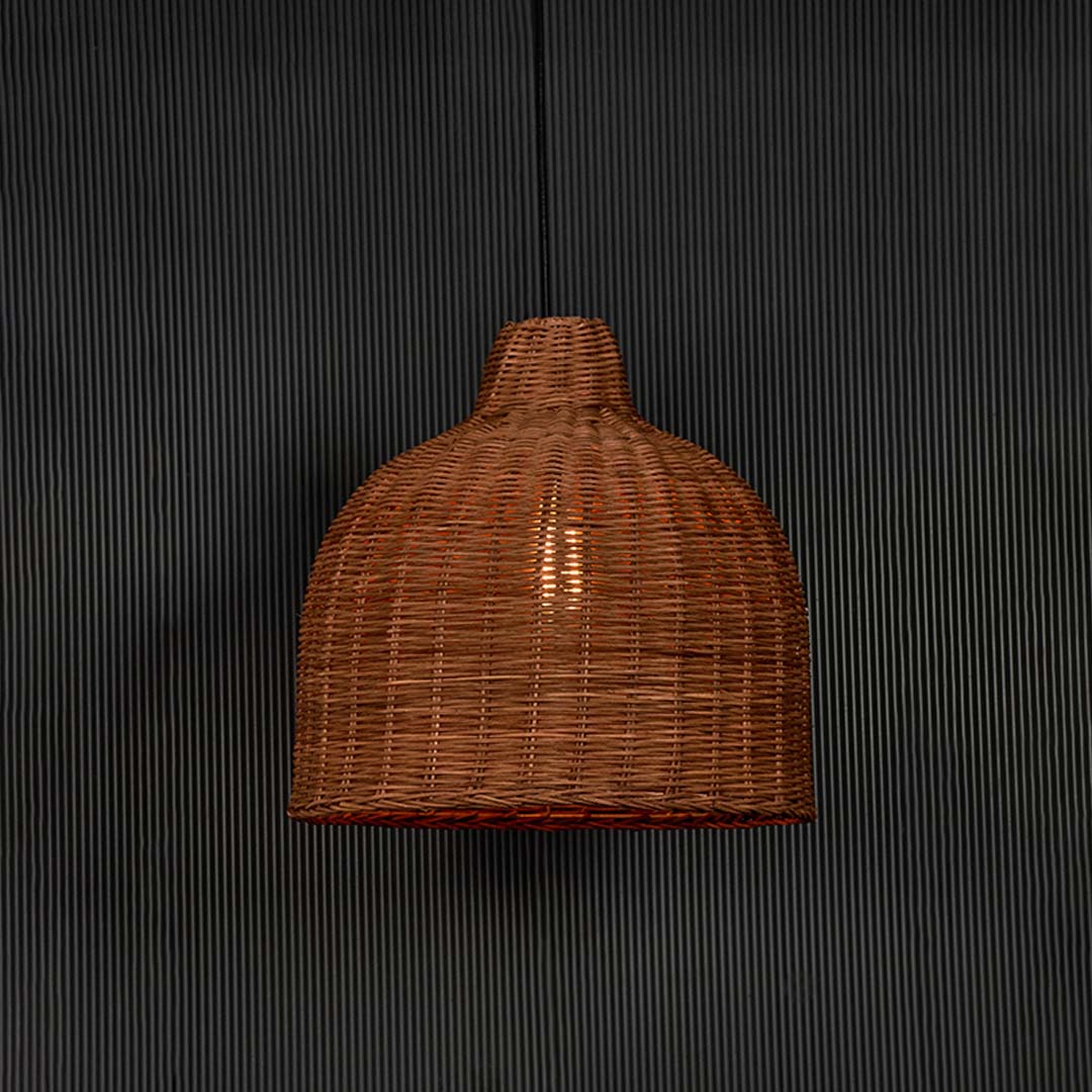 Rattan pendant light glowing on black background with natural wicker dome shade for rustic boho style interiors.