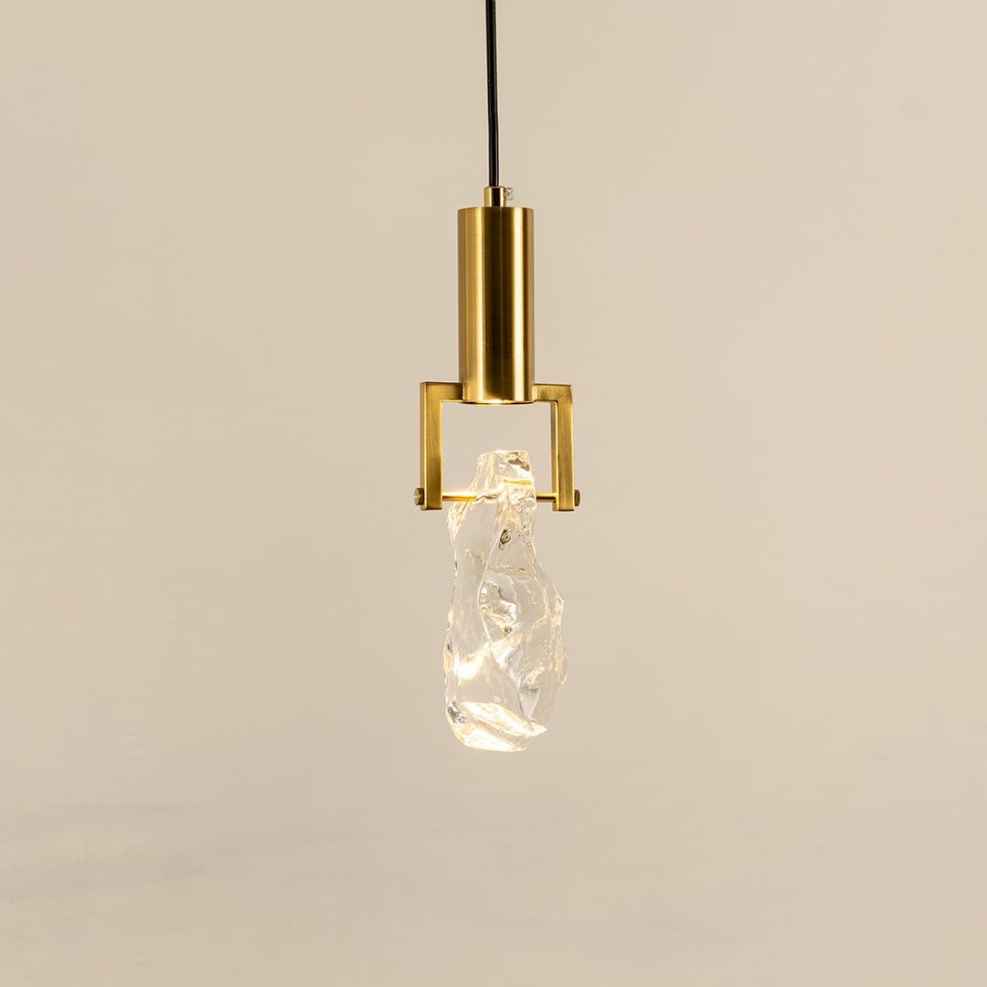 Contemporary hanging light with crystal-like glass shade and gold-toned metal base glowing softly against a white background perfect for modern decor.