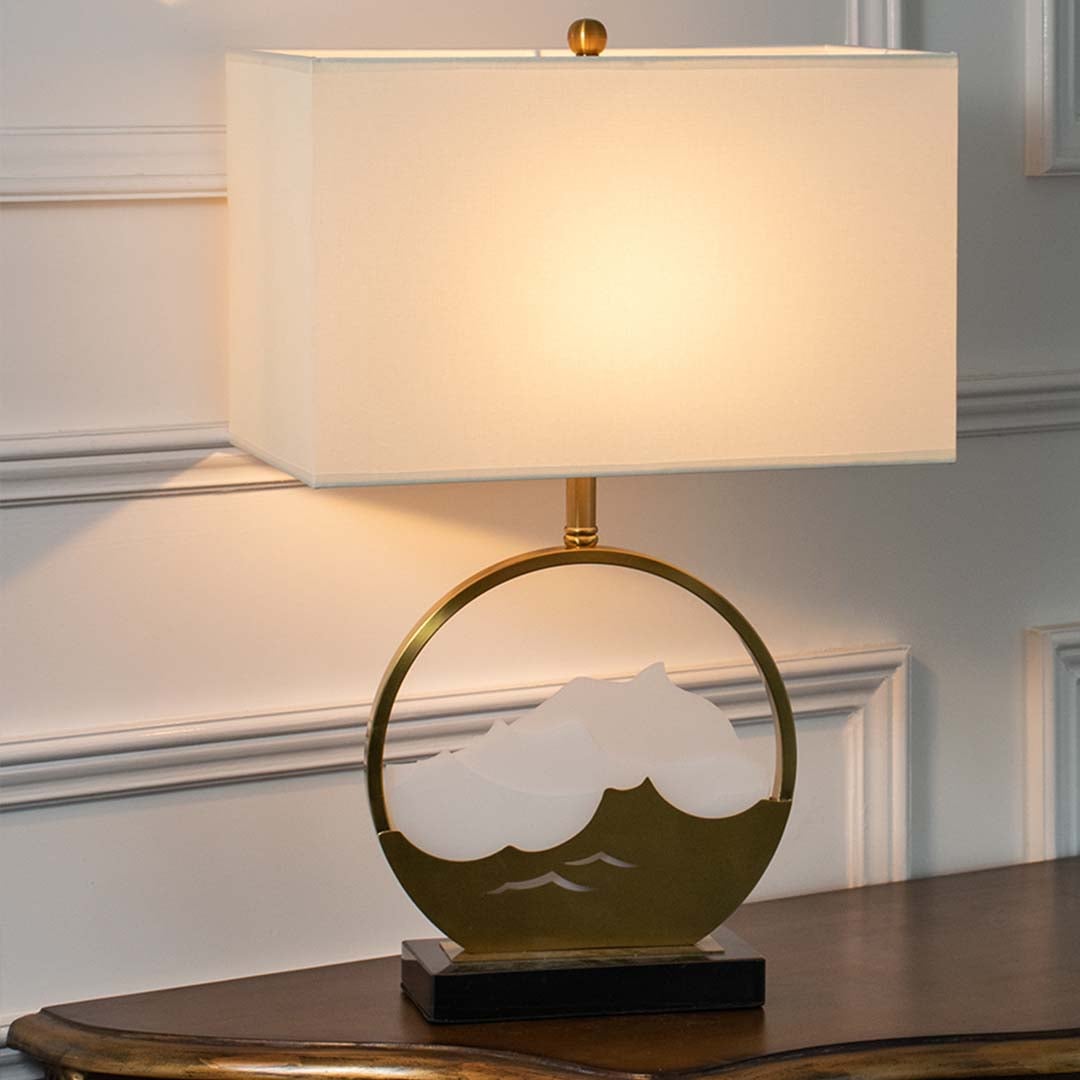 Gold metal table lamp with mountain inspired base and glowing rectangular fabric shade shown on a white background for elegant bedroom and living room lighting.