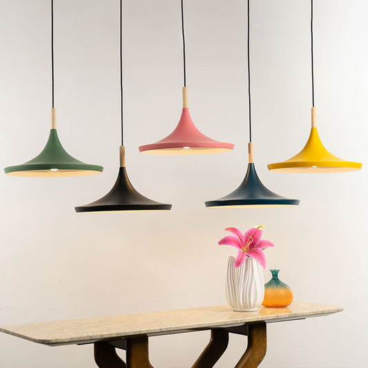 Colorful pendant lights in green black pink and yellow with wooden accents hanging above a dining table with decorative flowers.