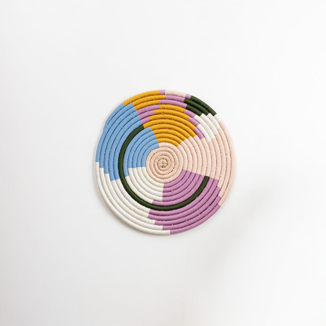 Round cotton woven wall plate in pastel blue pink mustard green and cream tones shown on a clean white background for modern artistic home wall decor styling.