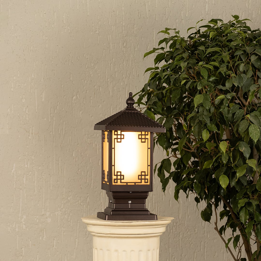 Black metal outdoor post lantern Light On mounted on a stone pillar Traditional garden gate lighting Main Lifestyle image at night.