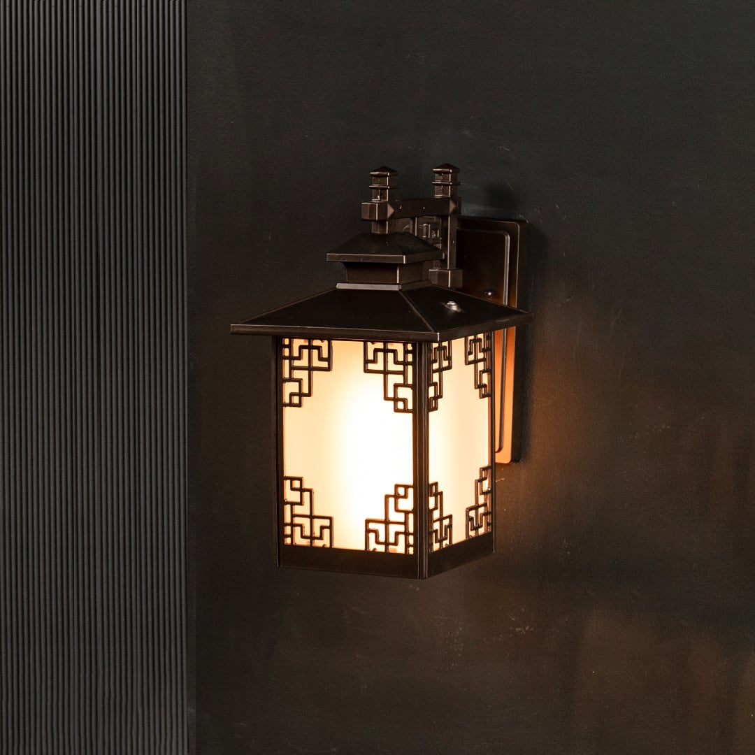 Brown metal outdoor lantern on black background with light on creating warm illumination through frosted glass and detailed geometric frame for exterior decor.