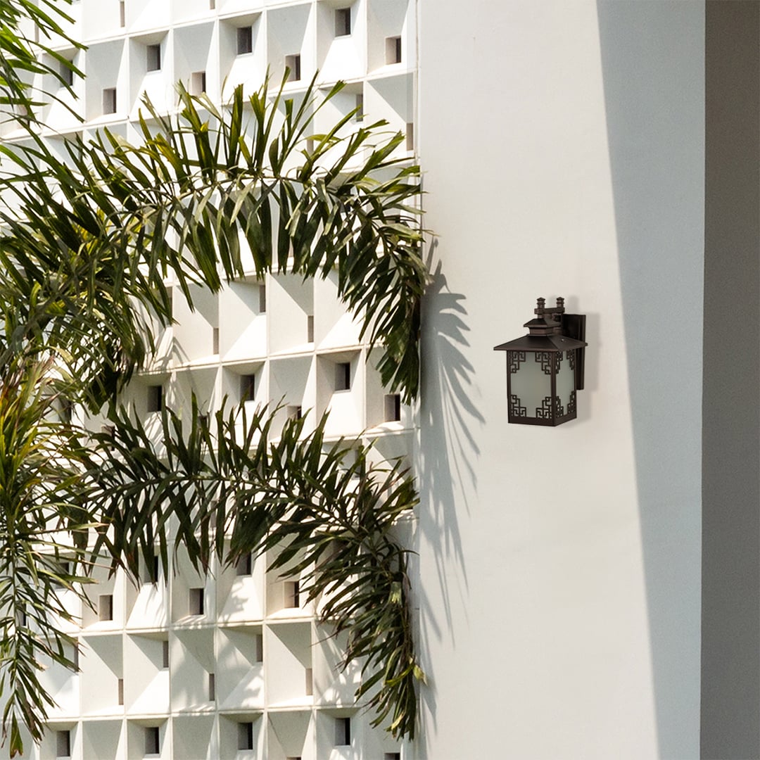Brown outdoor wall lantern fixed on a bright exterior wall with light off showing frosted glass panels and decorative metal design enhancing modern outdoor decor.
