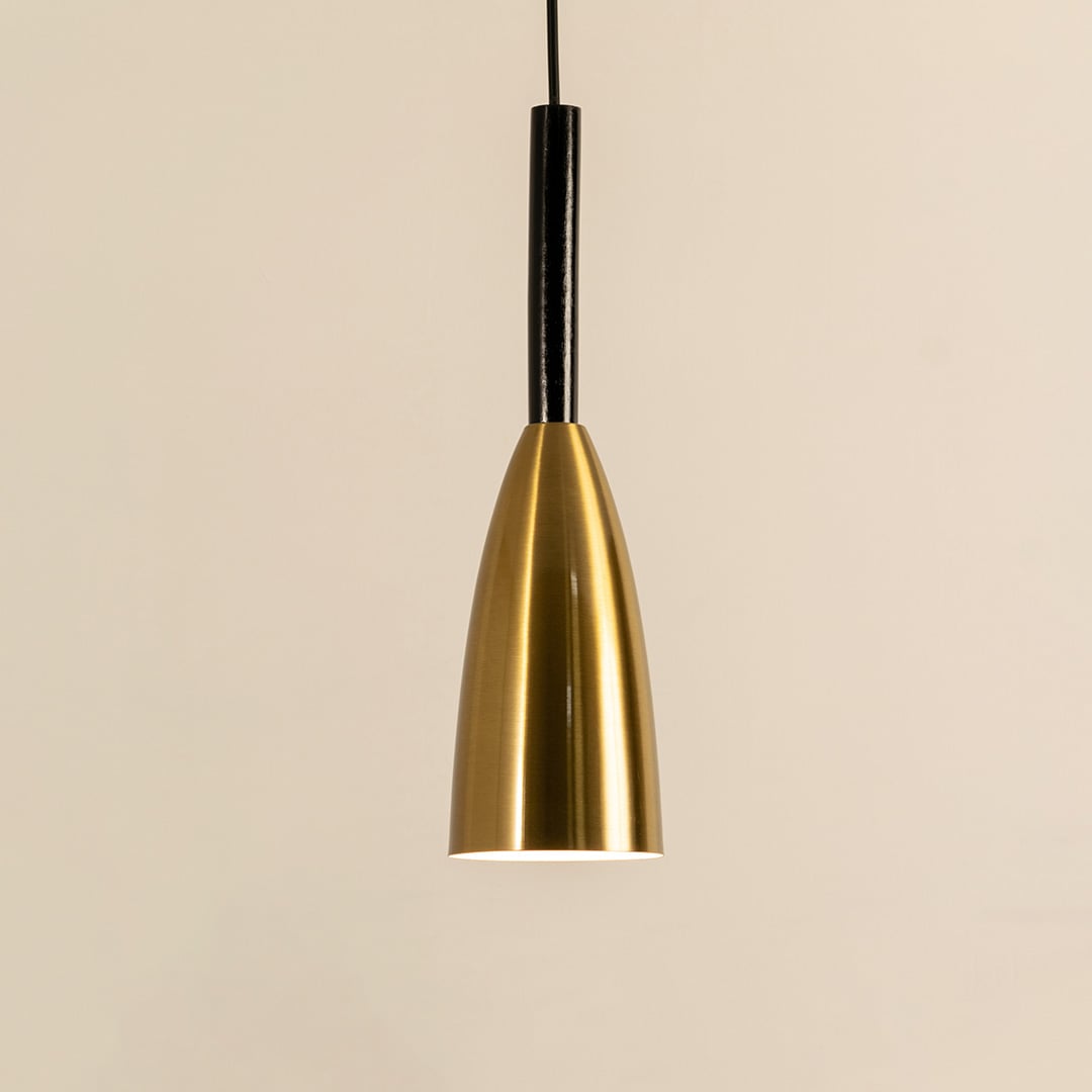 A slim metal pendant light glowing softly against a plain beige backdrop creating elegant focused lighting and minimal refined interior décor.